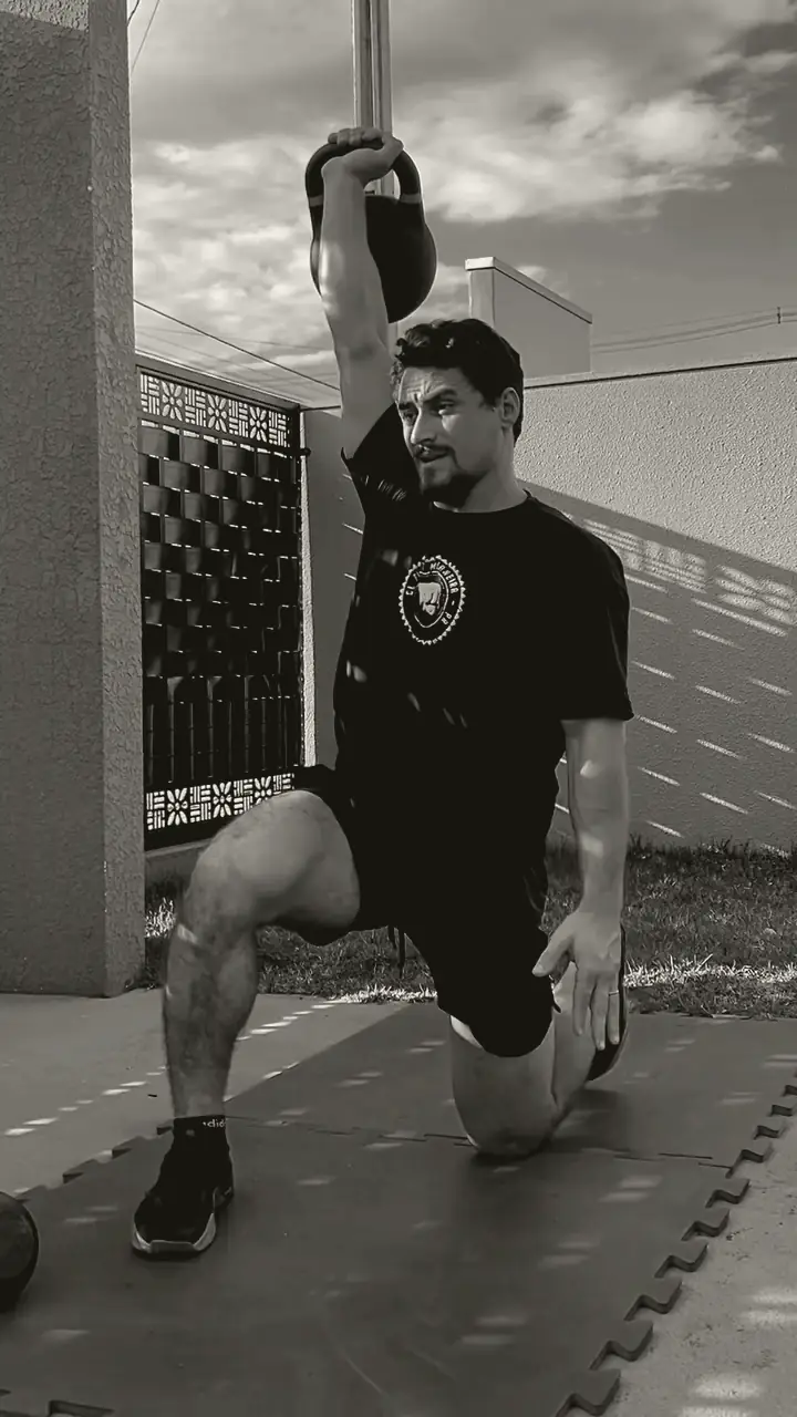 Lucas no meio de um turkish get up, ajoelhado com o kettlebell acima da cabeça