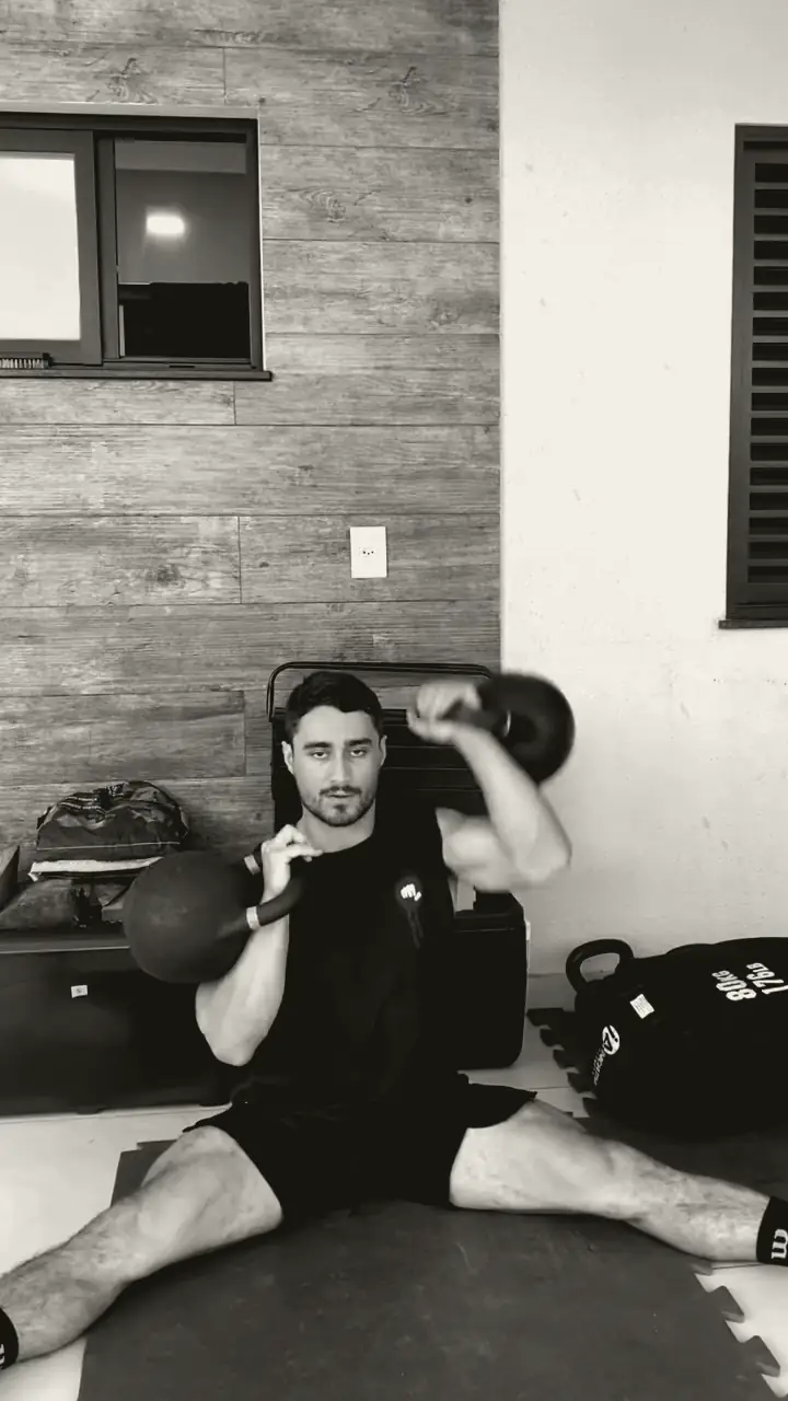 Lucas sentado no chão fazendo z-press com kettlebells